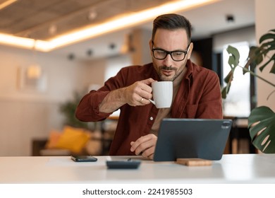 Stylish happy modern guy using tablet and drinking a cup of coffee. Photo of a male working on a tablet or reading news while drinking coffee. - Powered by Shutterstock