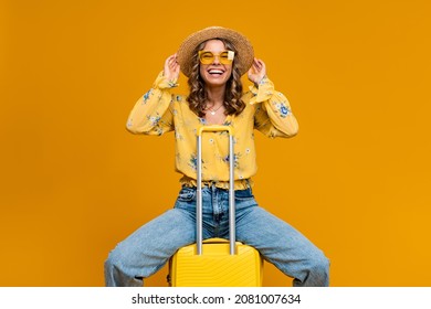 Stylish Happy Smiling Blond Woman Traveling With Suitcase Dressed In Trendy Outfit Jeans, Blouse And Hat, Sunglasses, Bright Yellow Background, Positive Summer Vacation, Fashion Trend