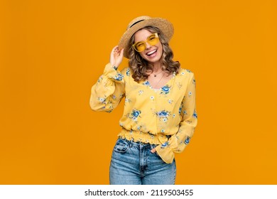 Stylish Happy Smiling Blond Woman On Vacation In Straw Hat Dressed In Trendy Outfit Jeans, Blouse And Sunglasses, Vibrant Yellow Studio Background Isolated, Positive Summer Mood, Fashion Trend