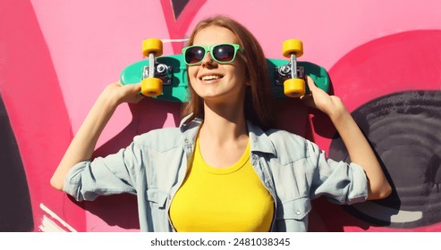 Stylish happy young girl with skateboard in glasses, modern teenager smiling girl looking away posing against the background of pink graffiti wall - Powered by Shutterstock