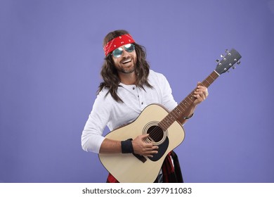 Stylish hippie man in sunglasses playing guitar on violet background