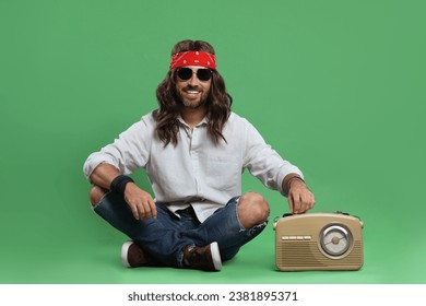 Stylish hippie man in sunglasses turning on radio receiver against green background