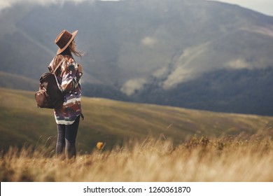 Stylish hipster girl in hat walking on top of mountains. Happy young woman with backpack exploring sunny mountains. Travel and wanderlust concept. Amazing atmospheric moment