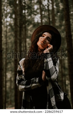 Stylish hipster girl in a hat wrapped in a checkered plaid posing in the base of a pine forest