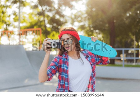Stylish hipster girl holding a skateboard and retro camera in hands on a bright sunny day. Youth concept. Summer lifestyle image of trendy pretty young girl 