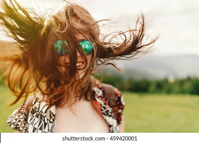stylish hipster woman traveler with fashionable sunglasses and windy hair smiling  and having fun on top of mountains in summer, travel concept, space for text. wanderlust