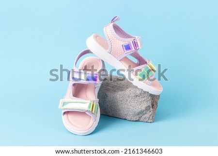 Stylish holographic sandals for kids on grey stone, blue background. Shiny fashion summer shoes. Front view.