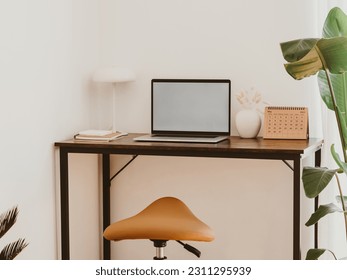 Stylish home office interior with laptop screen mockup, wooden table, plant, notes, saddle stool and elegant office accessories in designer apartment. - Shutterstock ID 2311295939