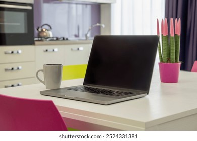 Stylish home office setup in kitchen with laptop, coffee mug, and decorative plant. Contemporary interior design showcasing remote work lifestyle and work-life balance in a bright home environment. - Powered by Shutterstock