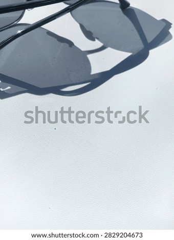 A stylish horizontal composition featuring chic sunglasses placed along the upper margin, casting distinct, soft-edged shadows over a clean white textured surface. The clever framing leaves a large portion of the lower layout open, providing an ideal canvas for graphic designers, copywriters, and marketers looking to insert promotional text or brand logos. Perfect for summer lifestyle advertisements, eyewear collections, e-commerce stores, and fashion magazines. The bright sunlight accentuates the fine details of the metal frames and tinted lenses, creating a vibrant yet peaceful atmosphere. This photograph combines commercial utility with modern aesthetic charm, delivering a polished, high-contrast visual asset that seamlessly adapts to diverse digital marketing needs, website backgrounds, and creative print media layouts with professional grace.