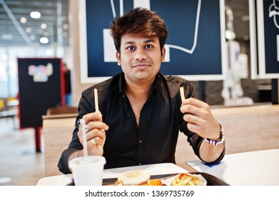 Stylish Indian Man Sitting At Fast Food Cafe And Eating French Fries.