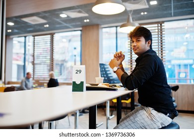 Stylish Indian Man Sitting At Fast Food Cafe Against His Laptop And Eating French Fries.