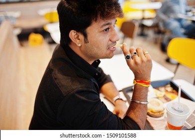 Stylish Indian Man Sitting At Fast Food Cafe And Eating French Fries.