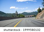 Stylish industrial long haul big rig bonnet semi truck transporting frozen commercial cargo in refrigerator semi trailer running for delivery on the overpass road with bridge across the Shasta Lake