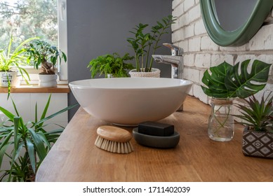 Stylish Interior Of Bathroom With Green Plants As A Natural Jungle And Window At Bright Home. Design Bathroom With Washbasin On Wooden Counter And Mirror. Close Up.