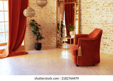 Stylish Interior With Burgundy Comfortable Armchair, Green House Plants In Pots, Coffee Table, Vintage Gold Mirror And Crystal Chandeliers Against A Brick Wall. Modern Living Room In French Style. 