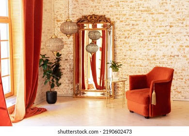 Stylish Interior With Burgundy Comfortable Armchair, Green House Plants In Pots, Coffee Table, Vintage Gold Mirror And Crystal Chandeliers Against A Brick Wall. Modern Living Room In French Style. 