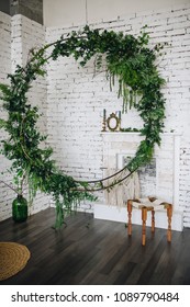 Stylish Interior. Decoration In The Form Of A Circle Of Greenery. White Brick Wall. Fireplace. A Candlestick And A Frame For A Photo.