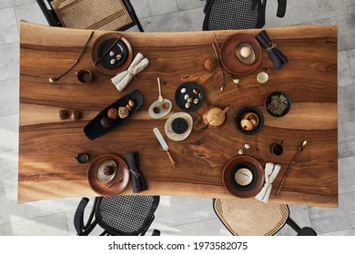 Stylish interior design of dining room with wooden walnut table, retro chairs, tableware, plates, tablecloth, teapot, food, decoration and elegant accessories. Cement floor. Template. Top view.