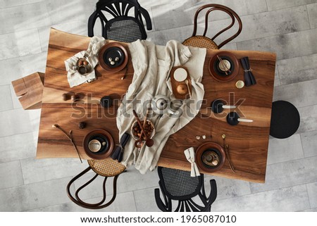 Stylish interior design of dining room with wooden walnut table, retro chairs, tableware, plates, tablecloth, teapot, food, decoration and elegant accessories. Cement floor. Template. Top view.