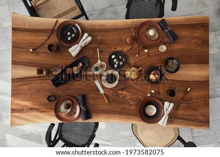 Stylish interior design of dining room with wooden walnut table, retro chairs, tableware, plates, tablecloth, teapot, food, decoration and elegant accessories. Cement floor. Template. Top view.