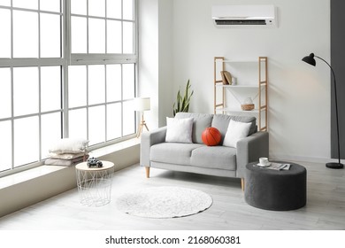 Stylish interior of light living room with sofa, shelf unit, pouf and air conditioner - Shutterstock ID 2168060381