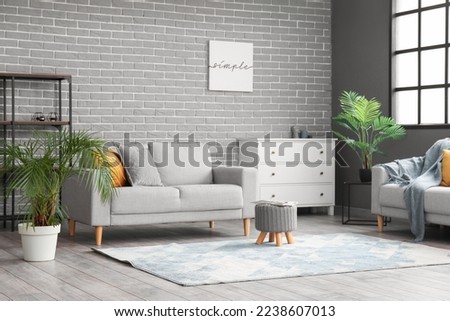 Stylish interior of living room with modern furniture near grey brick wall