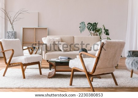 Stylish interior of living room with white cozy armchairs, sofa, coffee table, canvases, plants. Aesthetic Scandinavian home interior design.