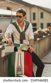 Stylish Italian Man Wearing White Shirt With Tied Sweater On Back Sitting On Scooter