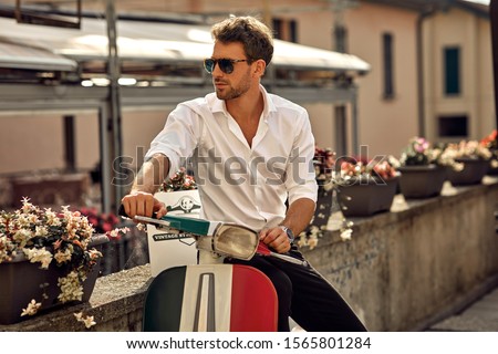 Stylish italian man wearing white shirt and sitting on classic scooter