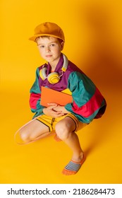 Stylish Kid Boy In 80s Sport Suit And Cap With Notebooks On Yellow Background