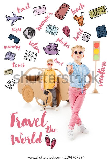 stylish kid in sunglasses showing thumb\
up while boy standing near cardboard car and traffic lights, with\
trip icons and \
