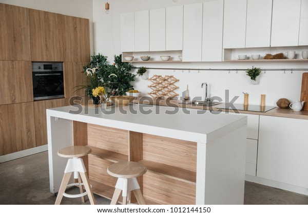Stylish\
kitchen in white and brown wood. Style minimalism. Sink, table top,\
plants, pot, shelf for dishes. Bar stools,\
table.