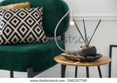 Stylish lamp and reed diffuser on side table near armchair with pillows indoors