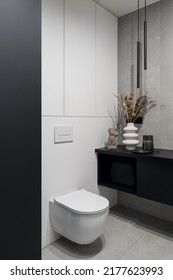 Stylish lavatory interior with white toilet, gray concrete style wall and floor tiles, modern lighting and decorations - Shutterstock ID 2177623993