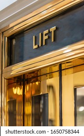 A Stylish 'Lift' Elevator Sign With Gold Lettering On A Dark Background Above A Golden Coloured Elevator Door