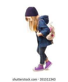 Stylish little girl in denim clothing, sneakers and backpack standing on a white background
