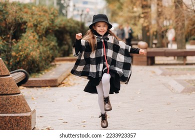 A stylish little girl in a hat walks around the autumn city - Shutterstock ID 2233923357