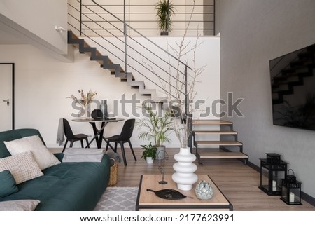 Stylish living room with dining table under staircase in two-floor apartment