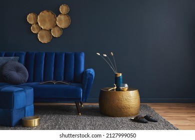 Stylish living room interior composition with velvet blue sofa, golden side table, pouf, pillows and elegant home decor. Dark blue wallpaper. Template. Copy space.