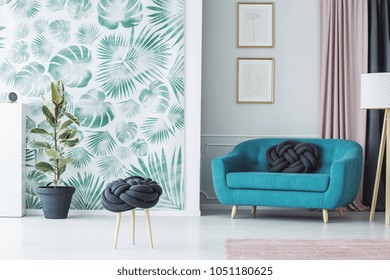 Stylish Living Room Interior With A Creative Knot Pillow Stool, Turquoise Sofa, Plant And A Wallpaper With Leaves