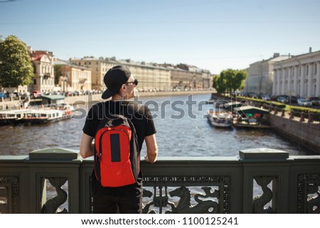 Stylish male tourist with backpack looking to cityscape on the embankment of Griboyedov canal in St. Petersburg, Russia.