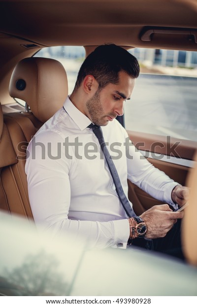 Stylish male in a white shirt using smartphone in a\
luxury car.