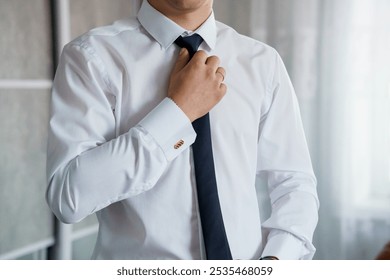 Stylish Man Adjusting Tie in Modern Indoor Setting. - Powered by Shutterstock