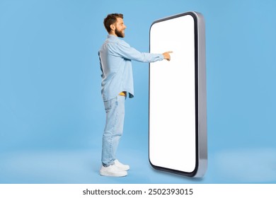 Stylish man in casual outfit touching large blank smartphone screen over blue studio background, checking mobile app or website, copy space, mockup - Powered by Shutterstock