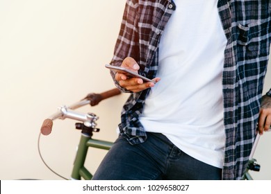 Stylish man chatting while using mobile phone while sitting on bicycle, outdoors. Dressed up in plaid shirt, t-shirt and jeans. Close-up. - Powered by Shutterstock