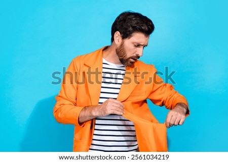 Stylish man in orange jacket checking pocket with teal background. Captivating blend of vibrant colors and modern fashion.