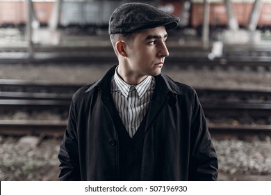 stylish man in retro outfit posing on background of railway. england in 1920s theme. fashionable look of brutal confident man. atmospheric moments.