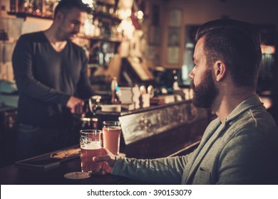 Stylish Man Sitting Alone At Bar Counter With A Pint Of Light Beer. 