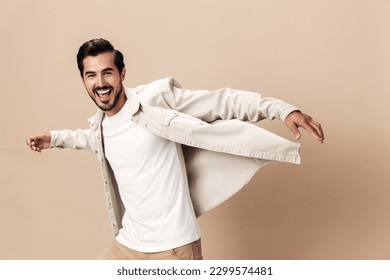 Stylish man smile runs and jumps on a beige background in a white t-shirt and business jacket, flying clothes hero, fashionable clothing style, copy space, space for text - Shutterstock ID 2299574481